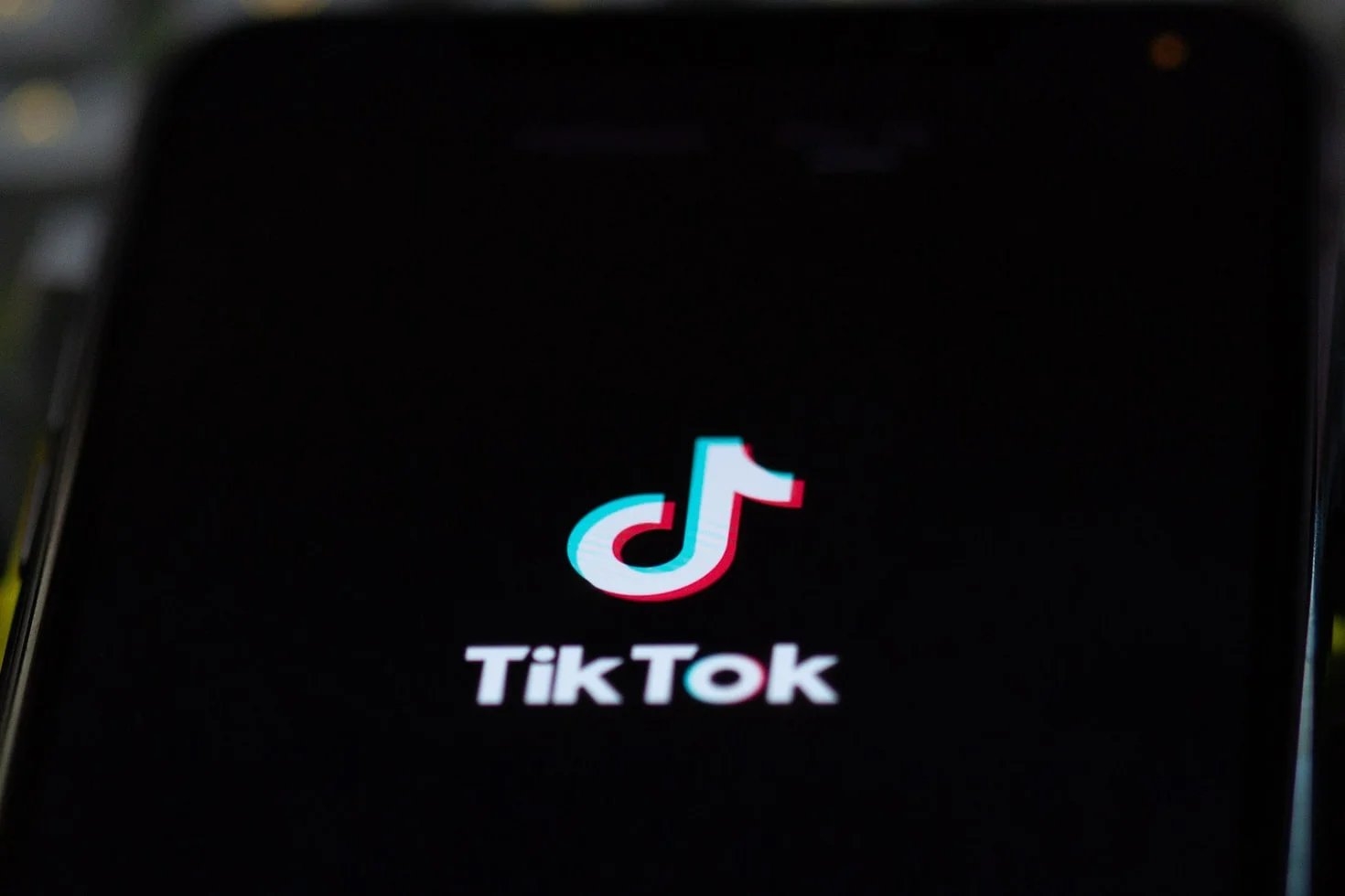 A person holding a smartphone, a TikTok logo visible on the screen