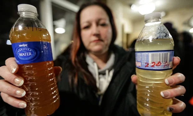 Child holds cup of discolored water, symbolizing Flint's ongoing water crisis