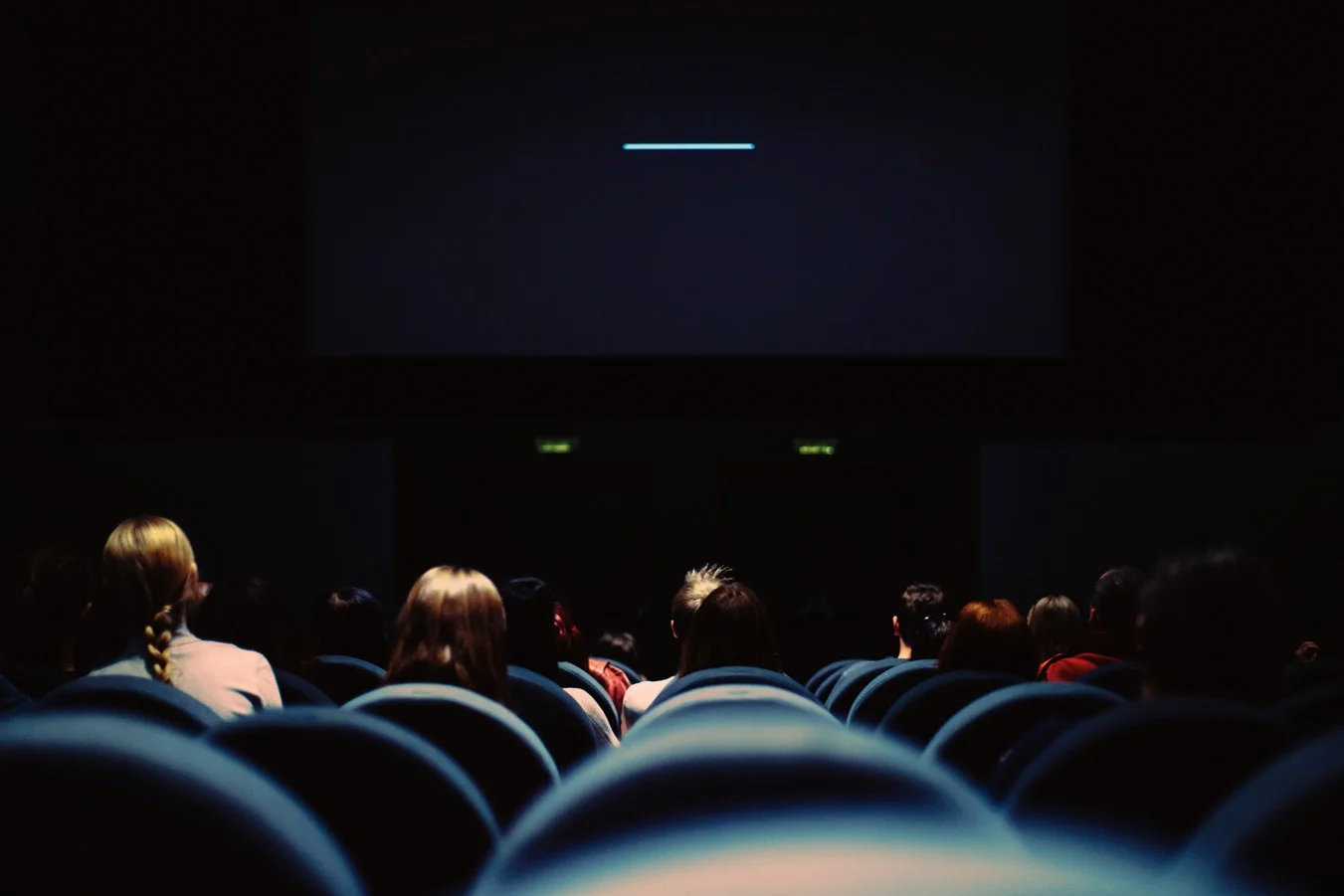 Man in theater seat with popcorn and drink, looking stressed at his phone
