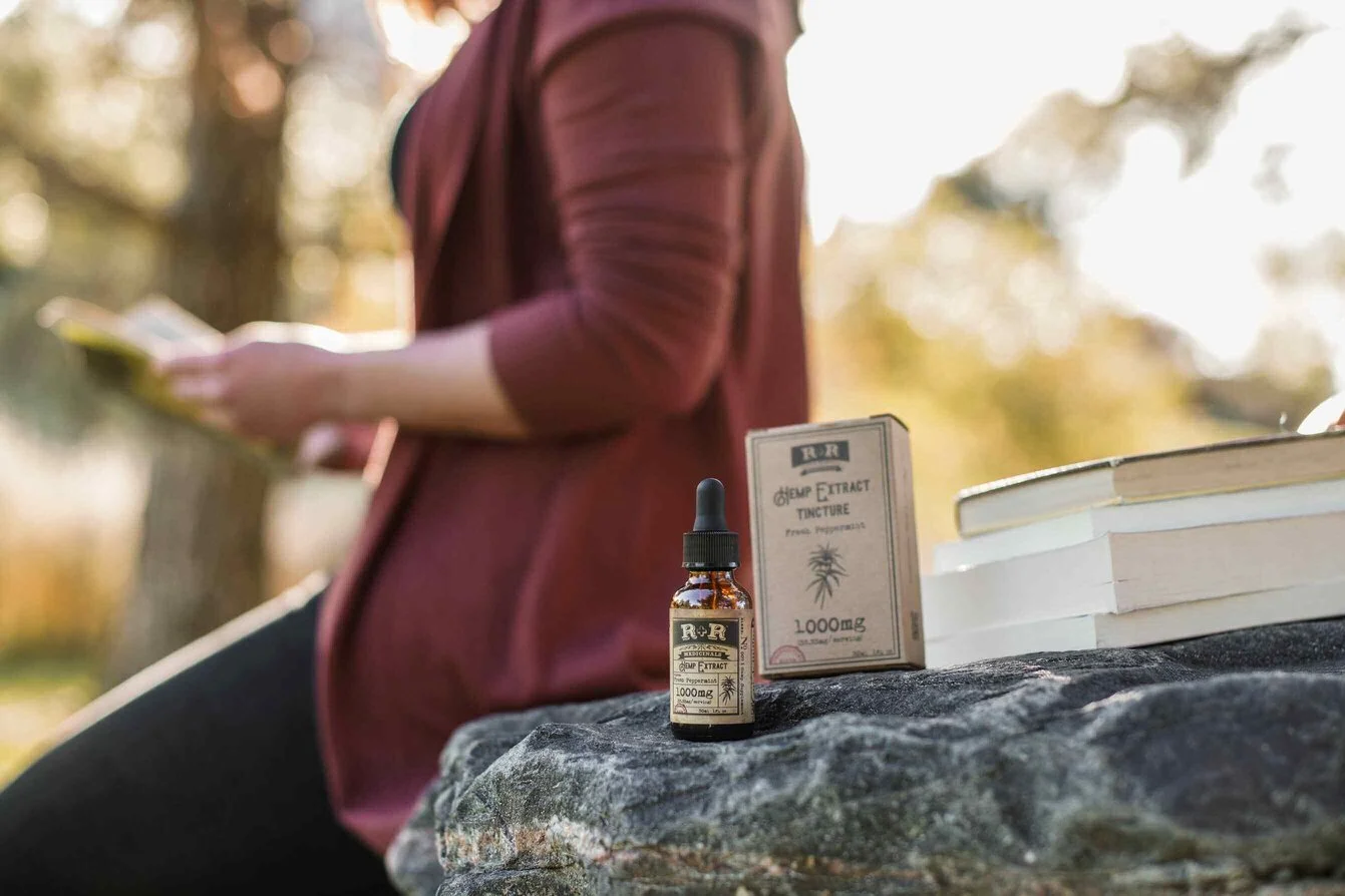 A CBD oil bottle next to a green leaf on a light-colored surface