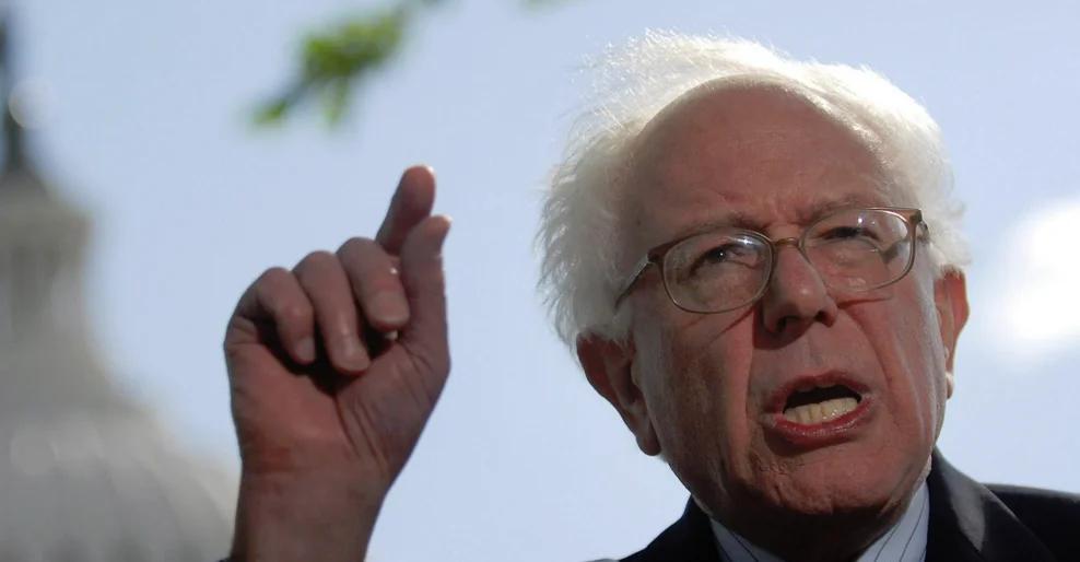 A senior man enthusiastically gesturing while speaking to a diverse audience at a town hall