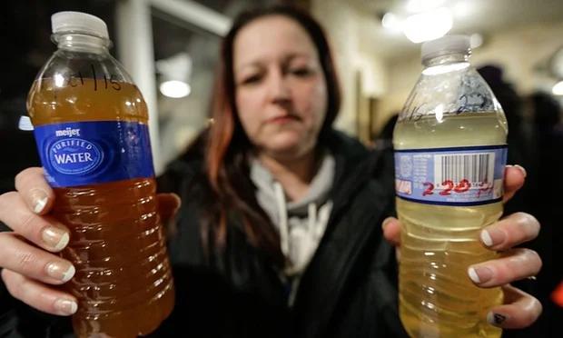Child holds cup of discolored water, symbolizing Flint's ongoing water crisis