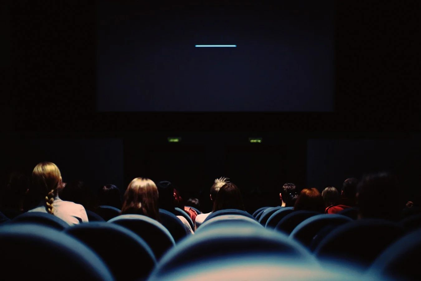 Man in theater seat with popcorn and drink, looking stressed at his phone