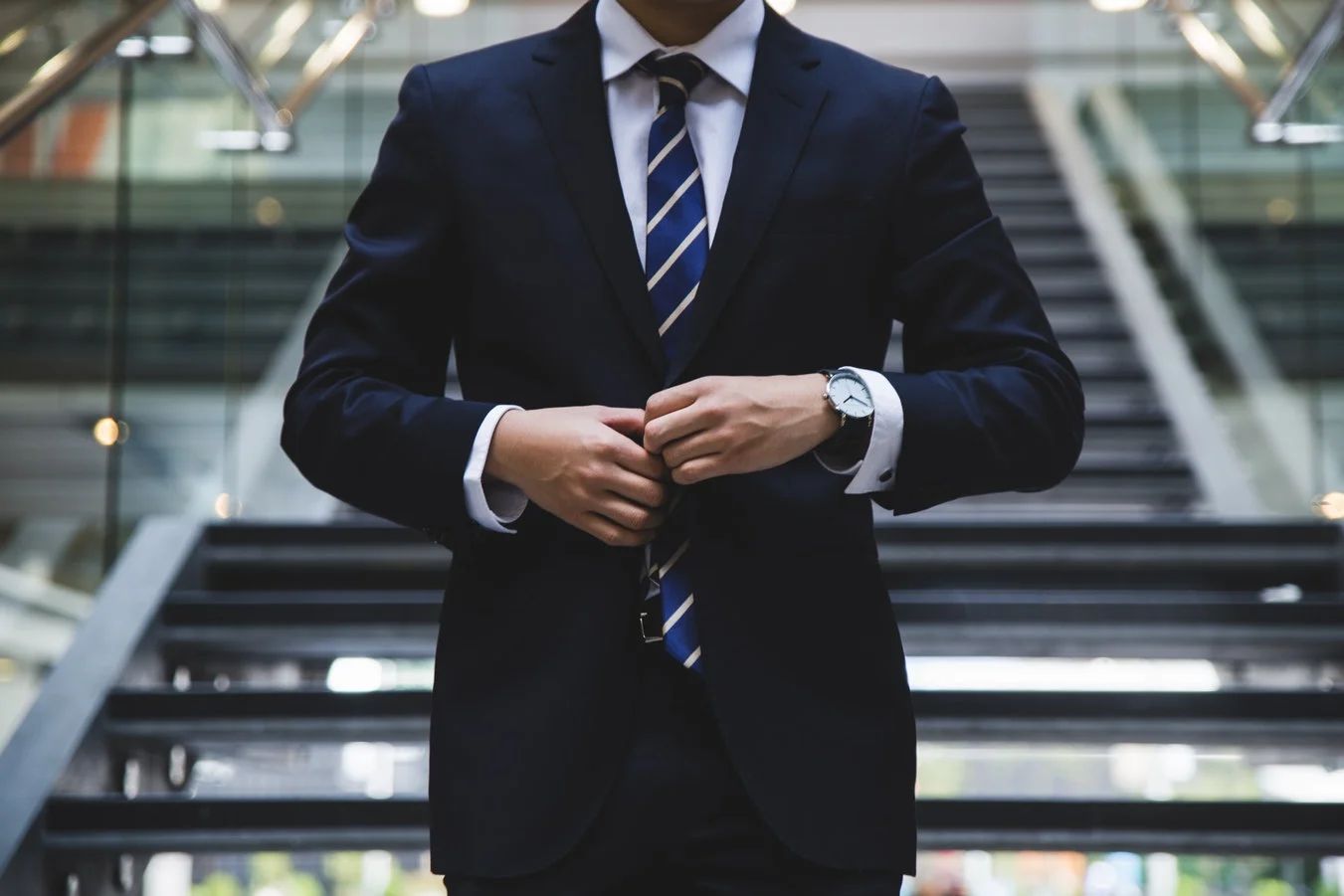 A woman in a blazer and glasses smiles, discussing PR strategies with colleagues